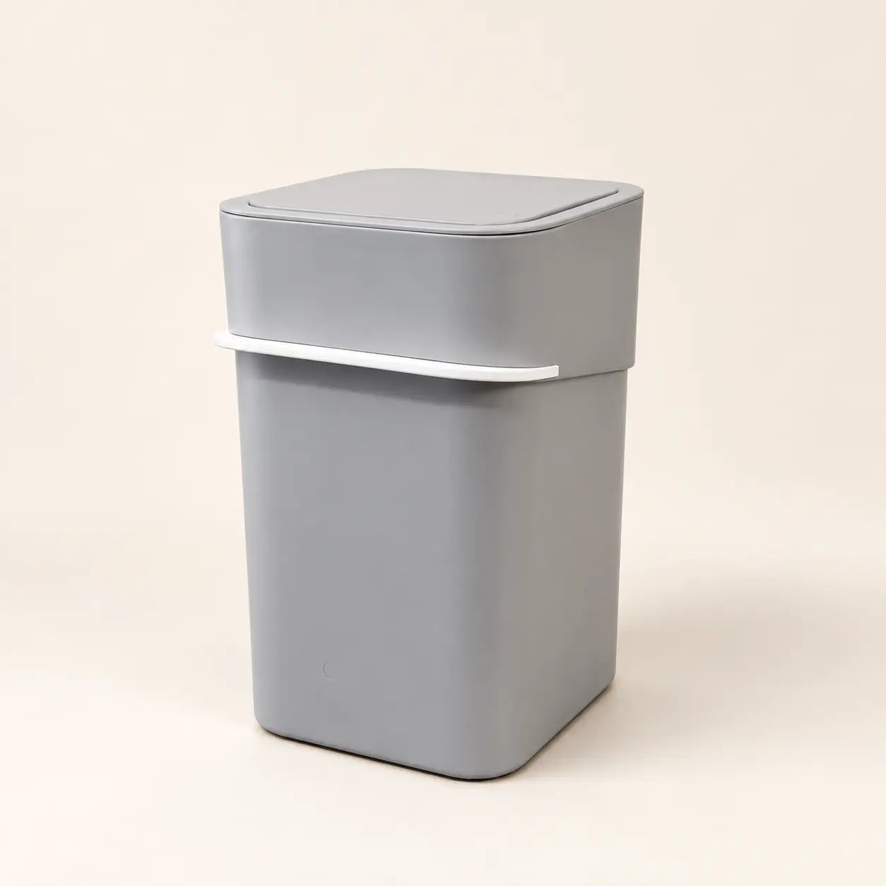Gray odor-control litter waste bin closed against a warm studio background